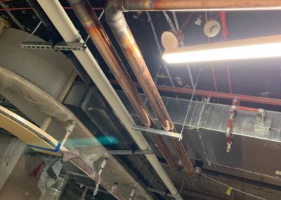 Copper and PVC plumbing pipes installed along a ceiling in an unfinished construction site.