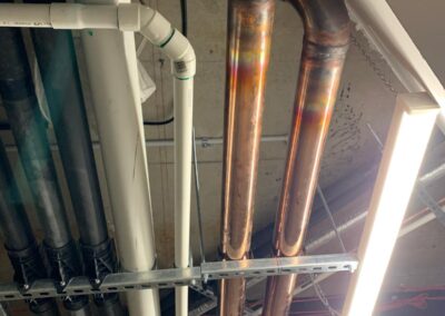 Ceiling-mounted copper and PVC plumbing pipes with a fluorescent light fixture nearby.