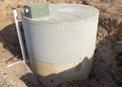 Concrete septic tank partially installed in a dug excavation site with an excavator in background. - Fosker Plumbing Western Sydney