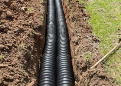 Two large black corrugated drainage pipes installed in a narrow trench beside green grass. - Fosker Plumbing Western Sydney