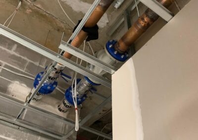 Copper pipes with blue flange fittings installed along concrete ceiling in building under construction. - Fosker Plumbing Western Sydney