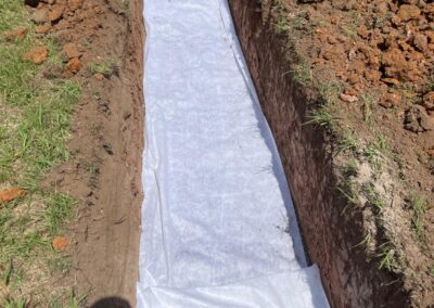 Long trench dug in soil with white geotextile fabric lining the bottom and sides. - Fosker Plumbing Western Sydney