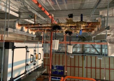 Exposed copper plumbing pipes with valves and hanging devices inside an industrial ceiling.