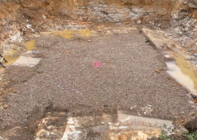 Excavated site with gravel and soil layers, marked for plumbing installation work.