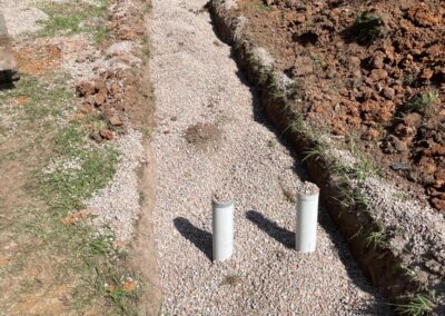 Excavated trench filled with gravel and two vertical white PVC pipes in grassy area. - Fosker Plumbing Western Sydney