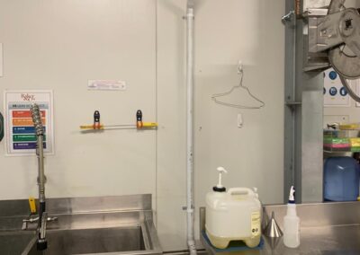 Stainless steel sink with tall faucet, plastic containers, and white PVC pipes mounted on wall. - Fosker Plumbing Western Sydney