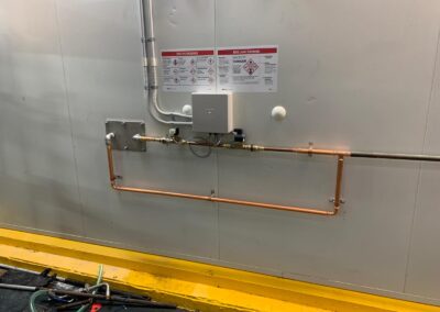 Copper piping system installed on a gray wall with safety labels and electrical wiring. - Fosker Plumbing Western Sydney
