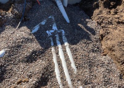 Underground plumbing pipes partially buried in gravel with exposed white PVC and orange conduit tubing.