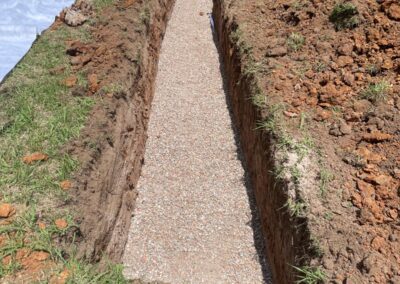 Narrow trench dug in grassy field with gravel base and piled soil on side. - Fosker Plumbing Western Sydney